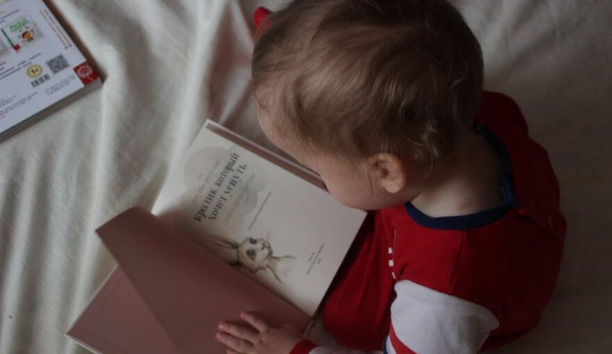 Cave Library Reading - baby sitting on bed while reading on book