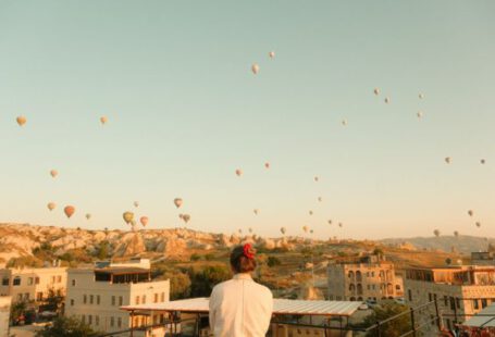 Göreme - a person standing on a balcony looking at hot air balloons in the sky