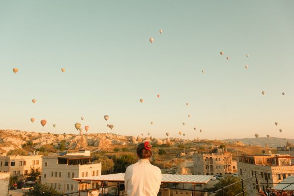 Göreme - a person standing on a balcony looking at hot air balloons in the sky