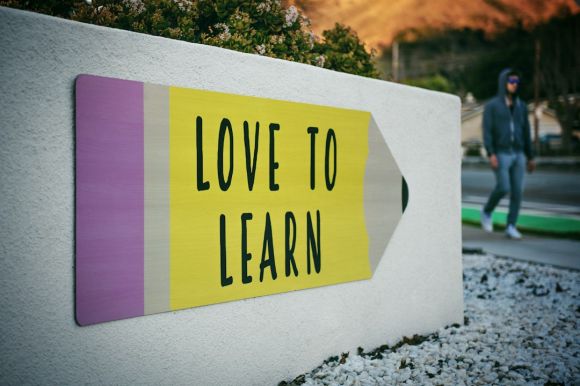 Learning Language - love to learn pencil signage on wall near walking man