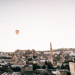 Picturesque scenery of old town with mosque placed among rocky formations in Cappadocia under flying hot air balloon in cloudless sky in daytime