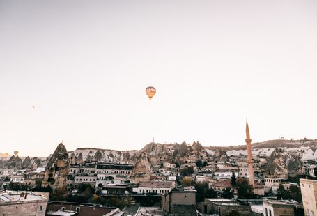 Picturesque scenery of old town with mosque placed among rocky formations in Cappadocia under flying hot air balloon in cloudless sky in daytime